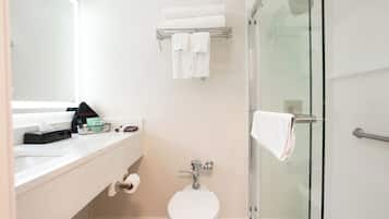 A bathroom with a toilet, a glass shower enclosure, a towel rack, and a sink with a towel dispenser.