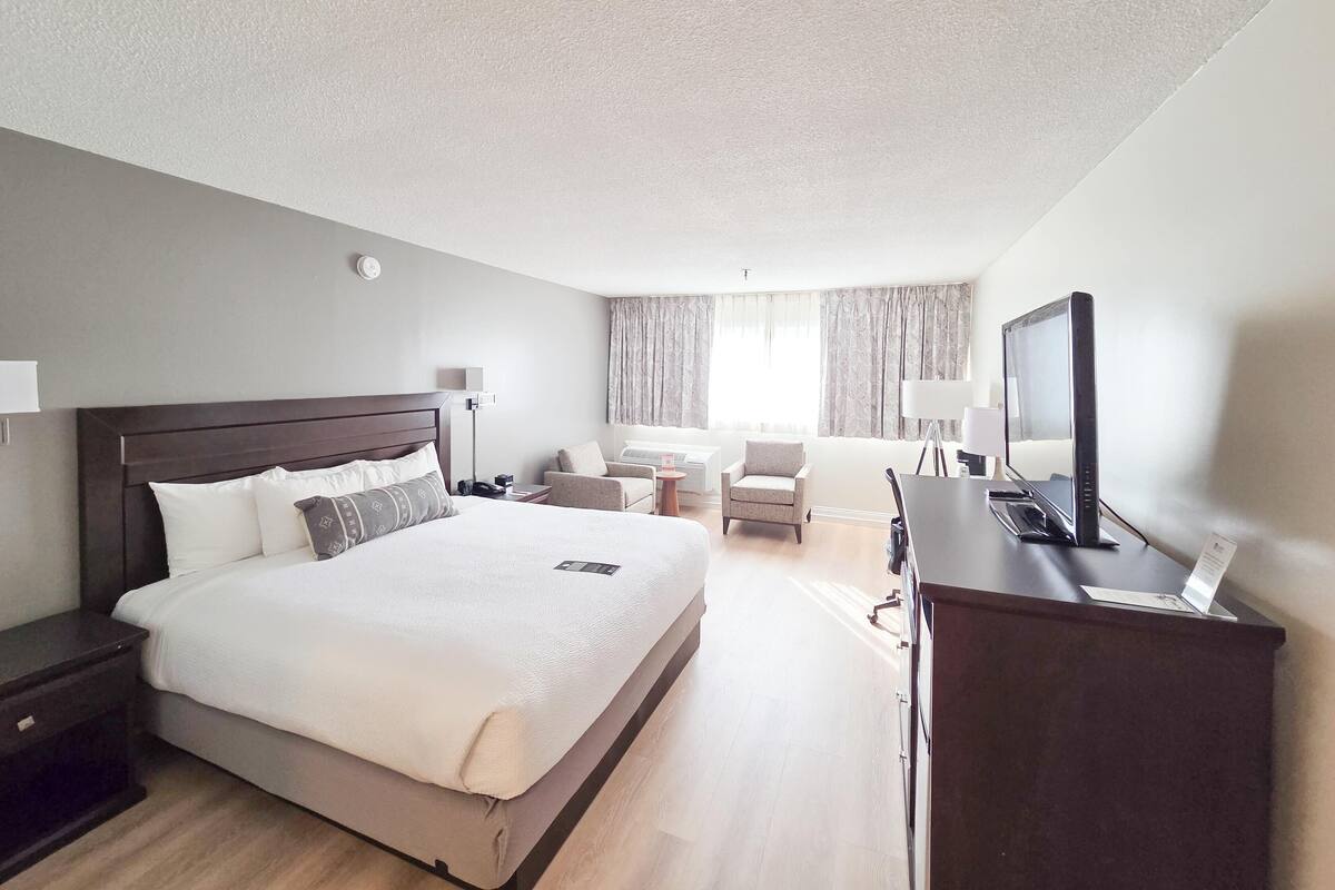 A hotel room with a large bed, bedside tables, a desk with a computer, a chair, and a television.