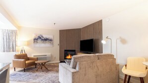 A living room with a sofa, armchair, TV, fireplace, and a lamp. - Fireside Inn & Suites Waterville (Waterville)