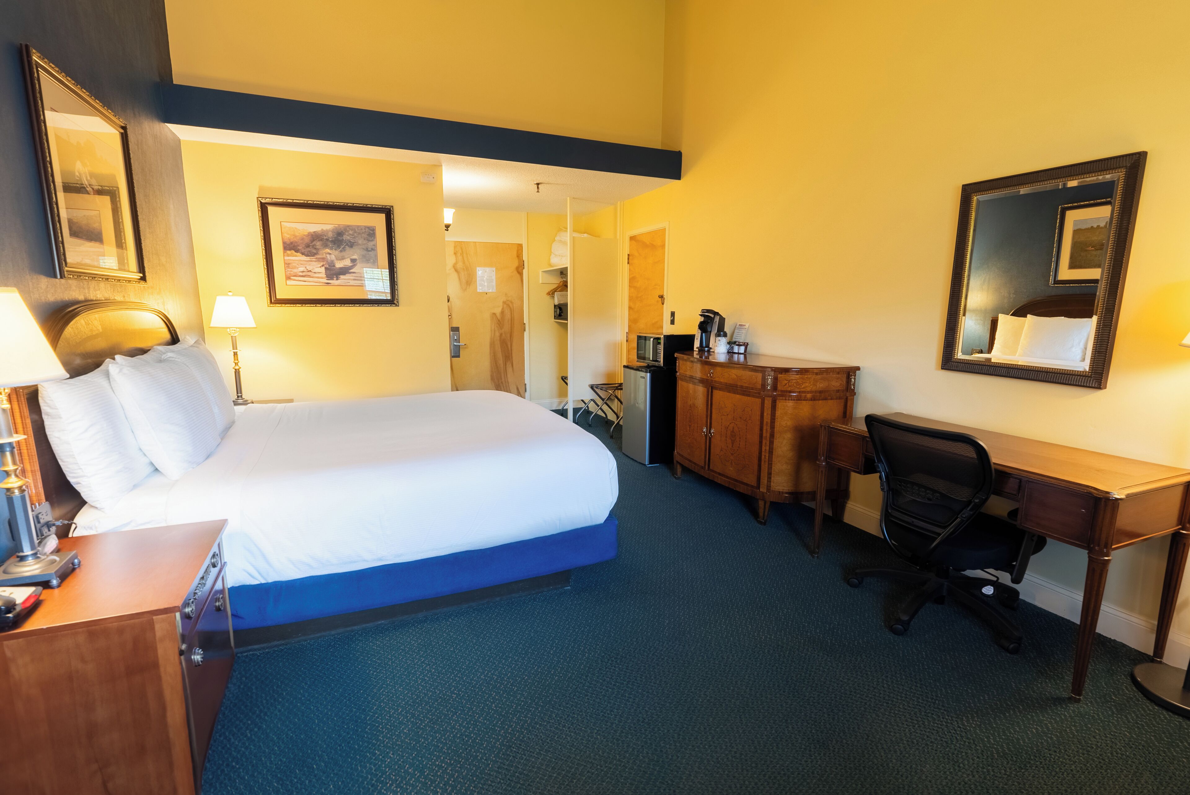 A hotel room with a bed, desk, chair, and a dresser.