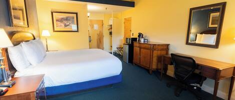 A hotel room with a bed, desk, chair, and a dresser.