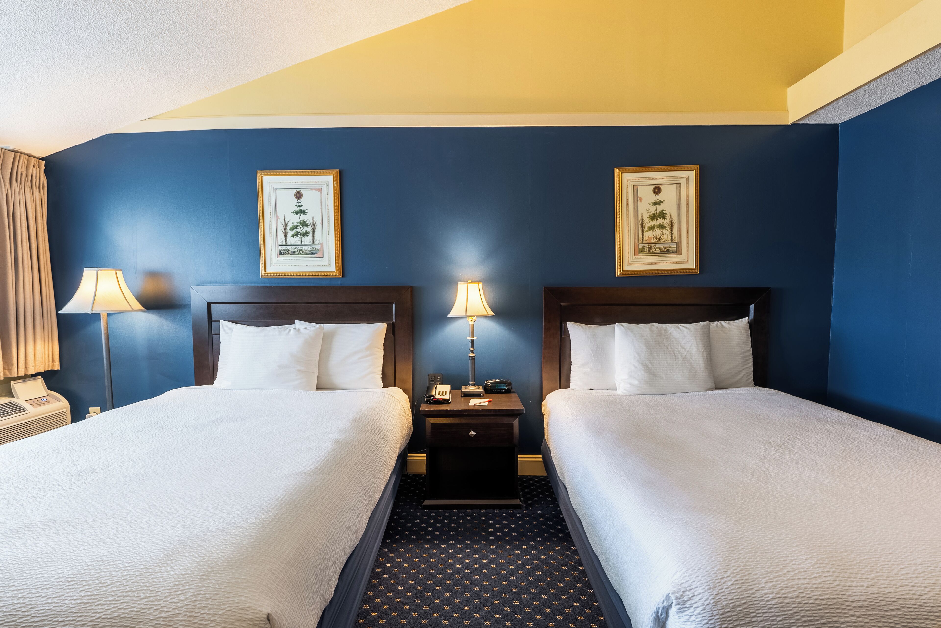 Une chambre d’hôtel avec deux lits, une table de chevet avec une lampe et des œuvres d’art encadrées accrochées au mur.