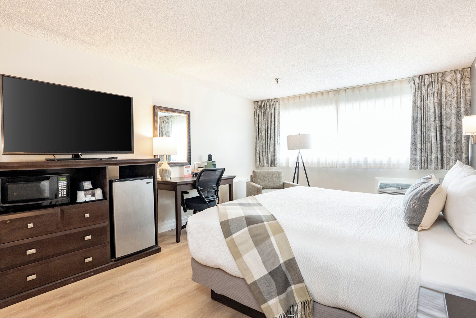 Habitación de hotel con cama, escritorio con silla, televisor, microondas y refrigerador pequeño.
