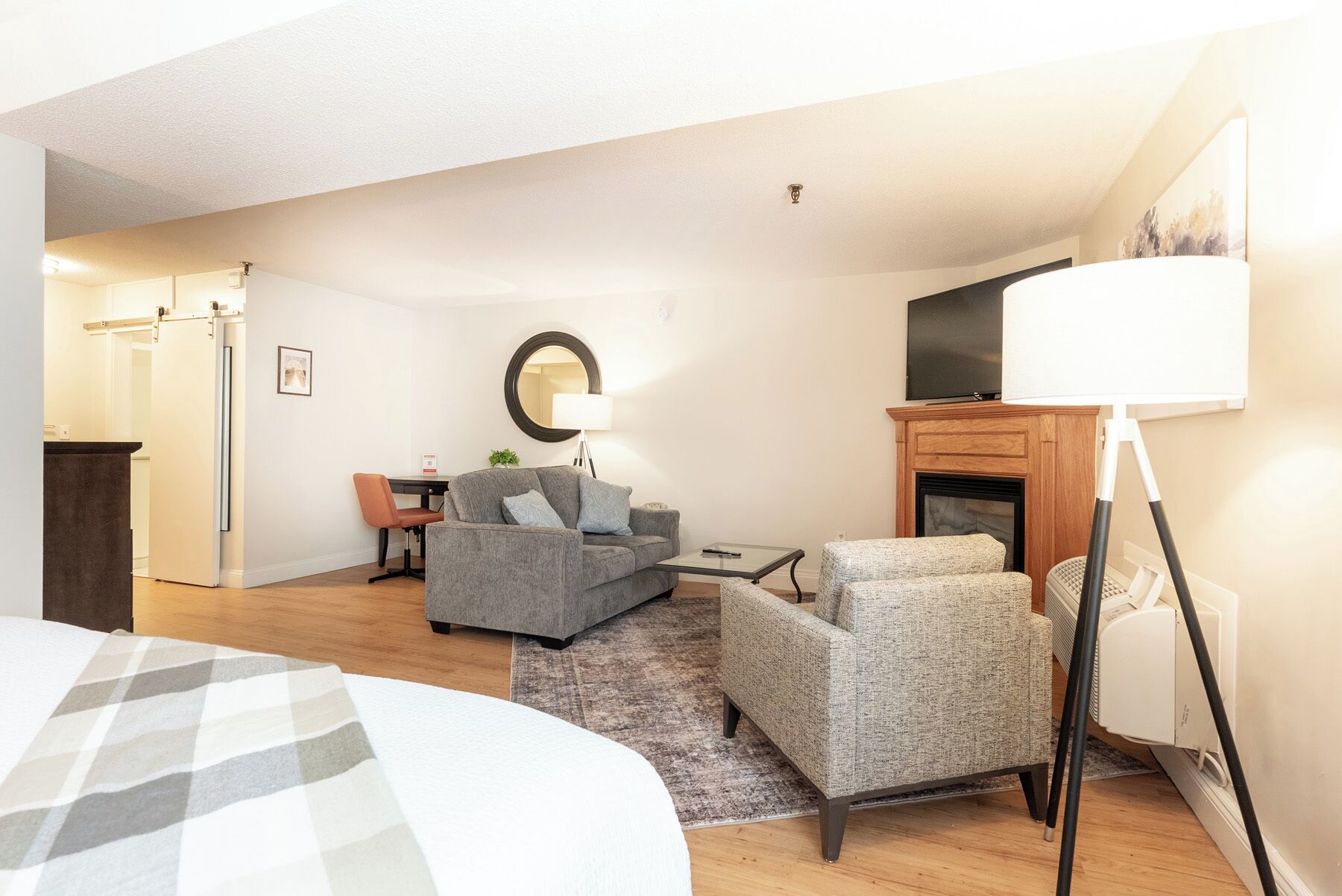 Ein modernes Hotelzimmer mit einem Bett, einem grauen Sofa, einem kleinen Tisch, einem Fernseher und einem Kamin.