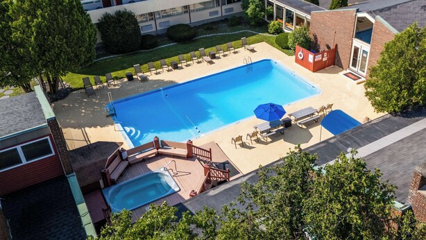 A rooftop swimming pool with lounge chairs and a hot tub, surrounded by trees and a parking lot.