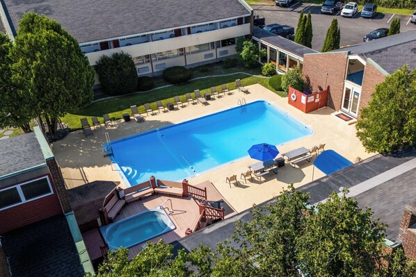 A rooftop swimming pool with lounge chairs and a hot tub, surrounded by trees and a parking lot.