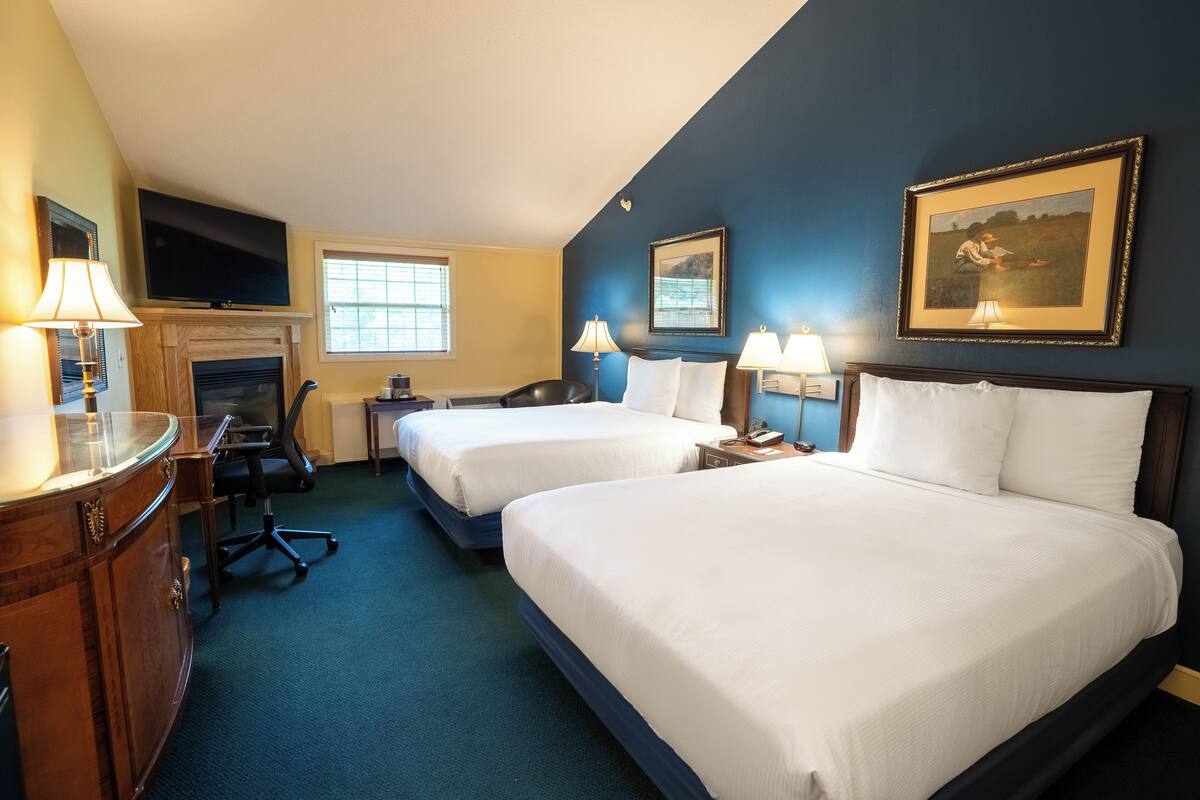 A hotel room with two beds, a TV, a desk, a chair, a lamp, and a painting on the wall.