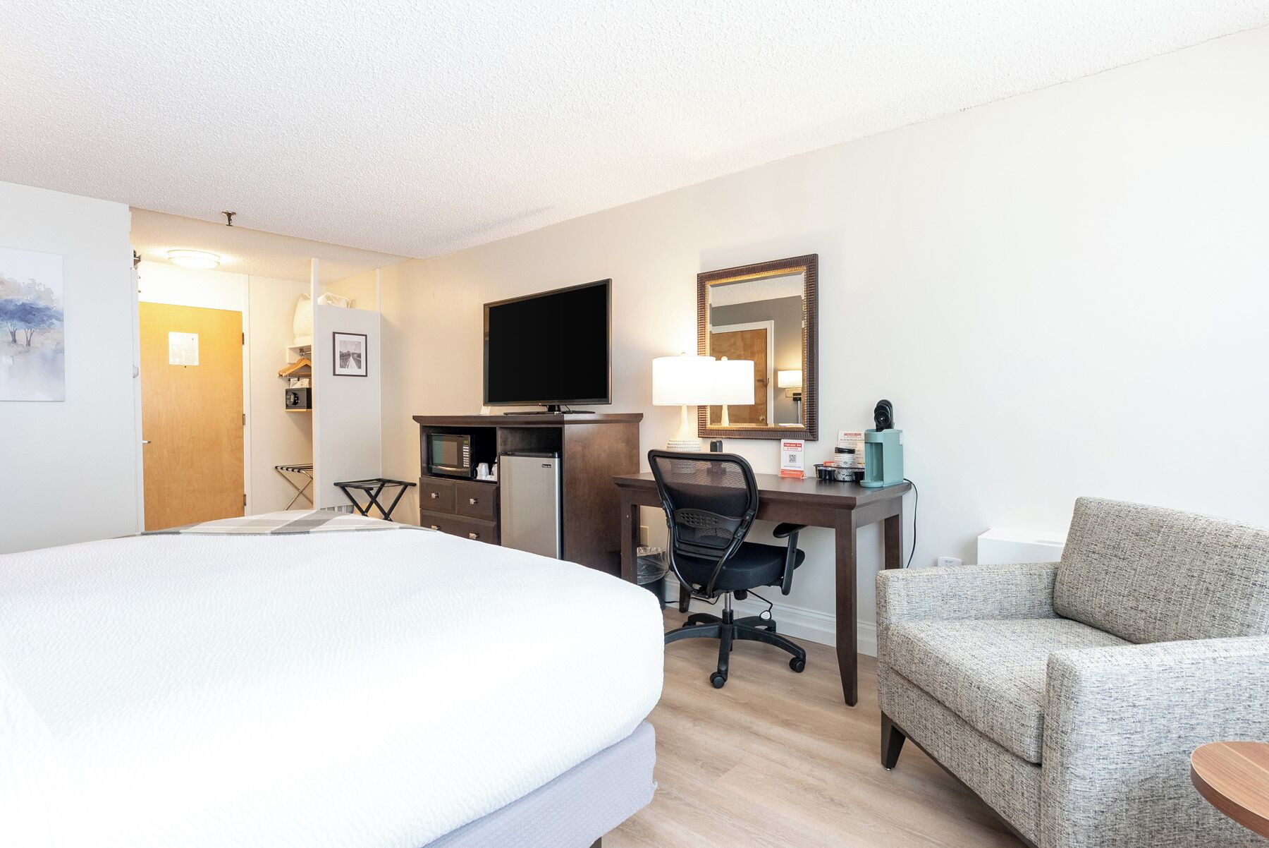 A hotel room with a bed, a desk with a computer, a chair, a couch, and a television.