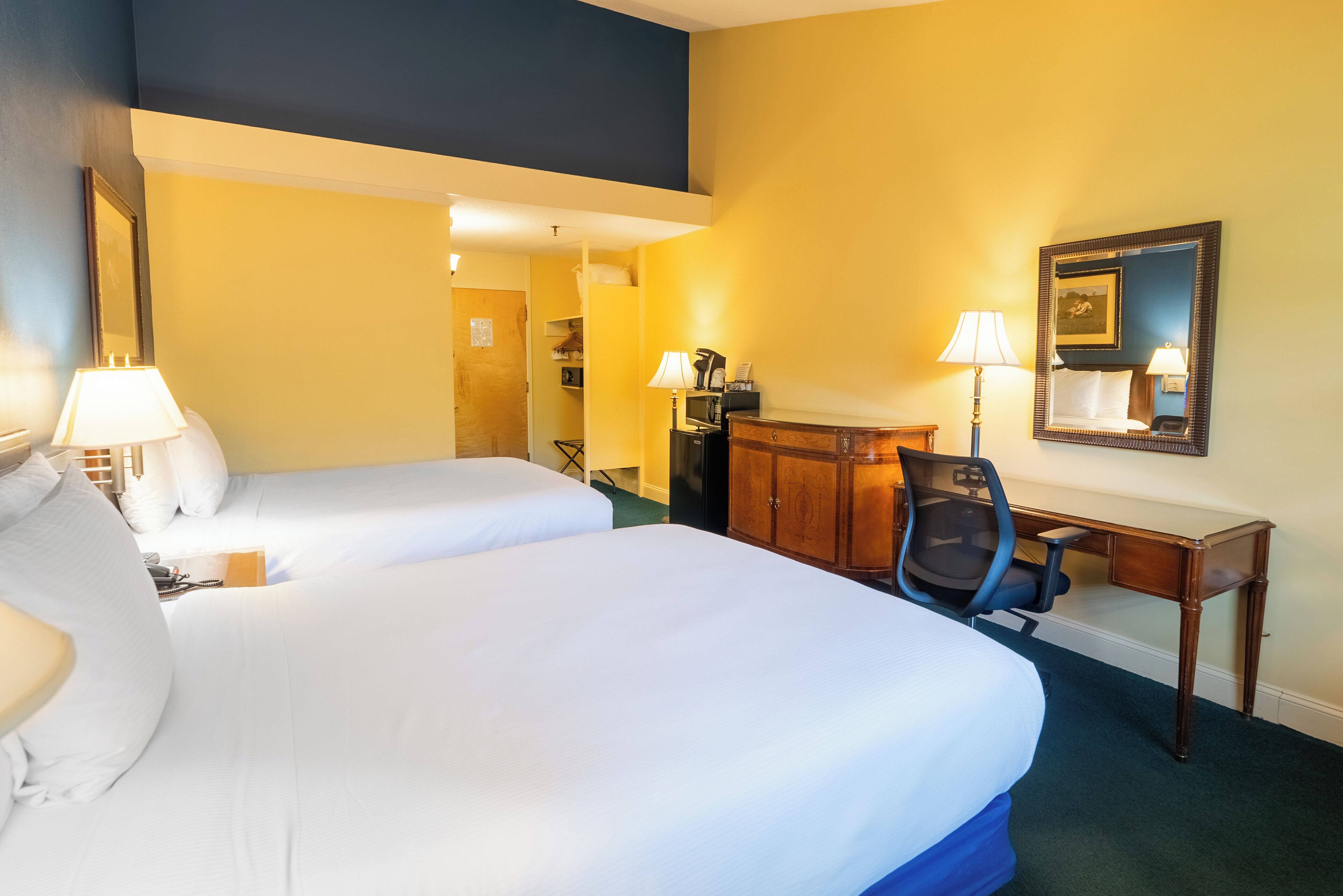 A hotel room with two beds, a desk, a chair, a dresser, and a mirror.