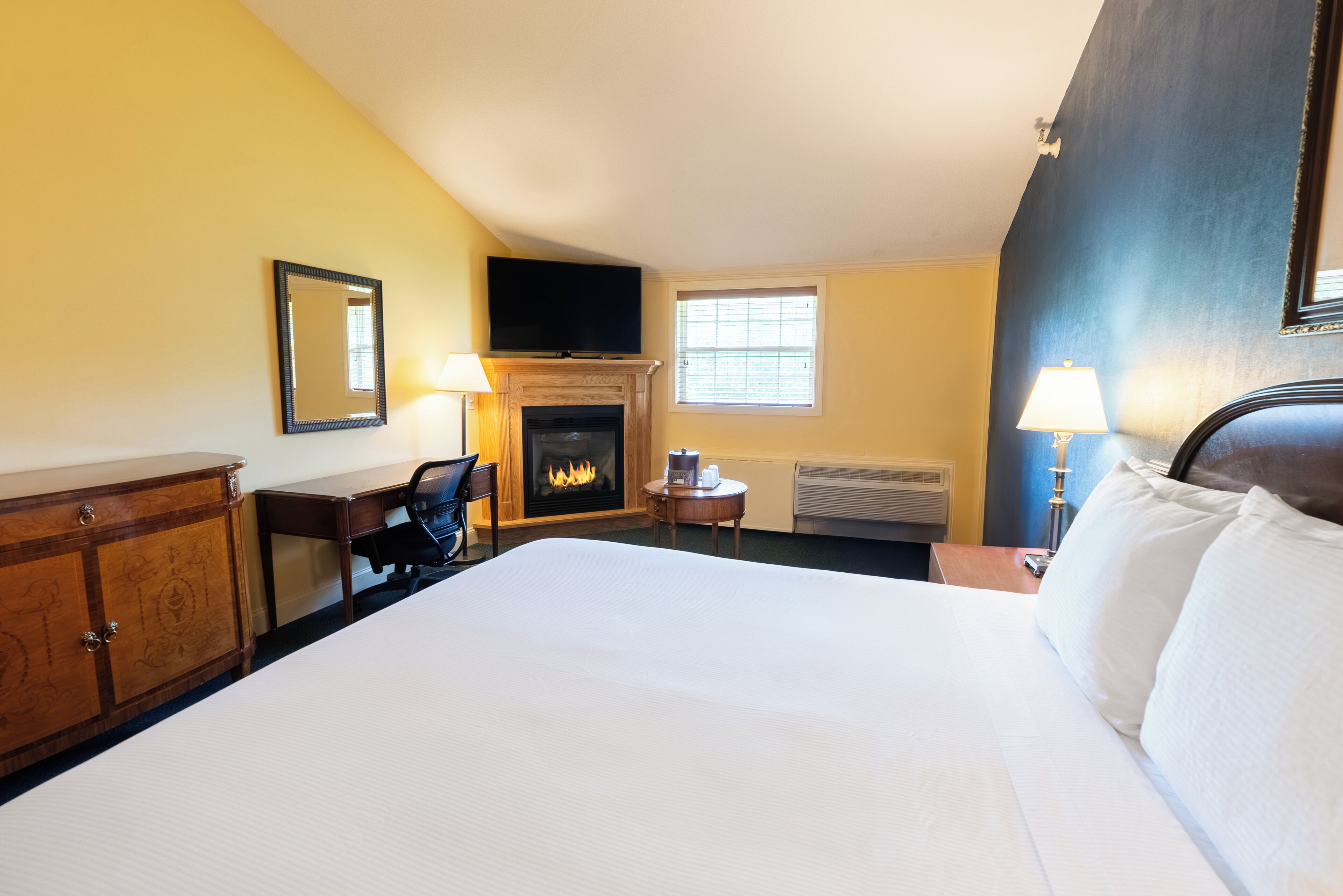 Una habitación de hotel con una cama grande, una chimenea, un escritorio y un televisor.