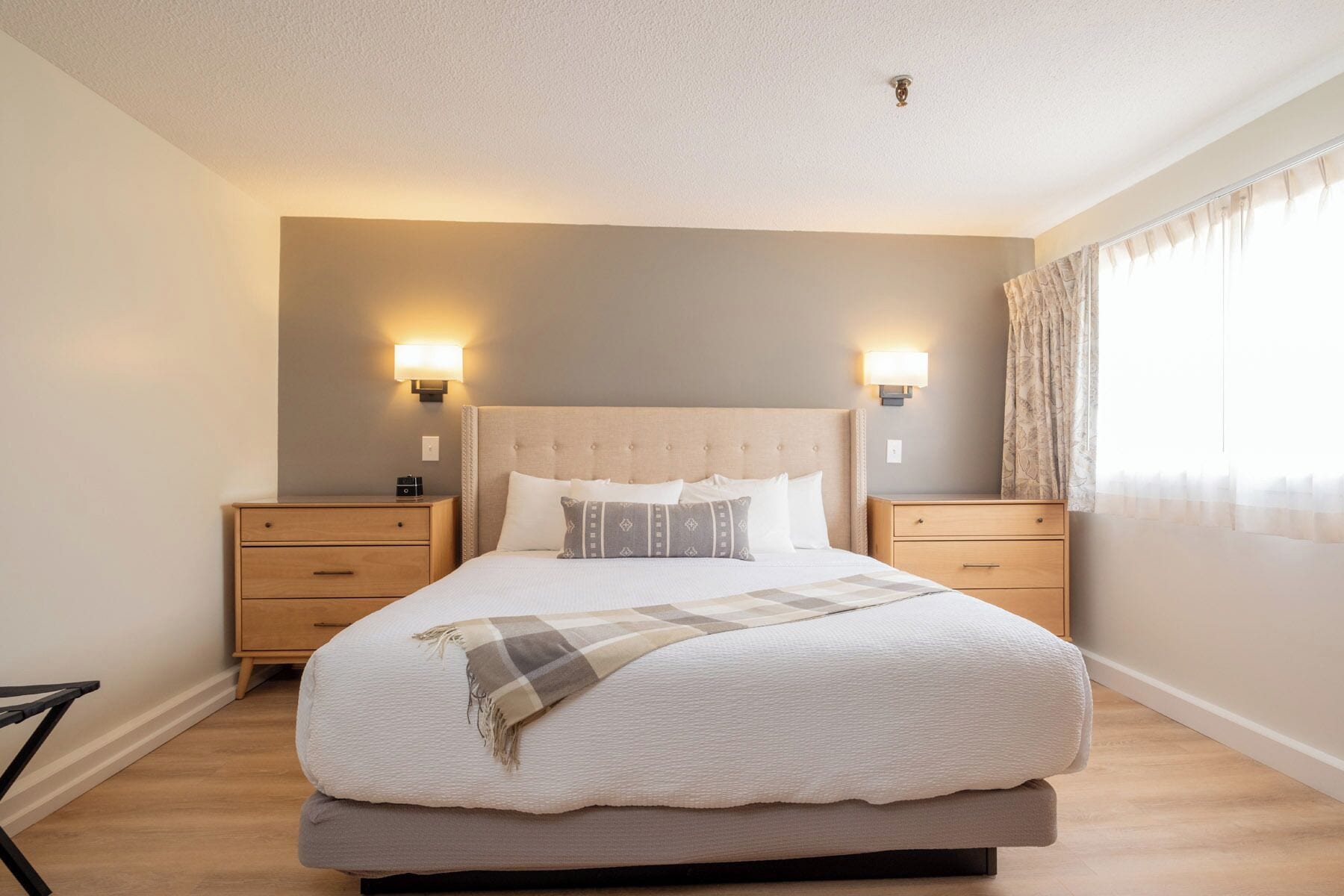 Un dormitorio con una cama grande, dos mesitas de noche, un cabecero y dos lámparas de pared.