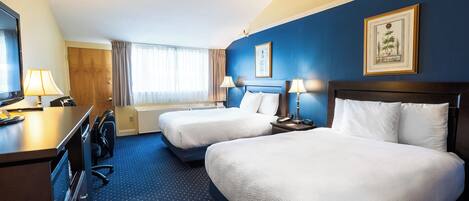 Une chambre d’hôtel avec deux lits, un bureau avec une lampe, une télévision et une fenêtre avec des rideaux.
