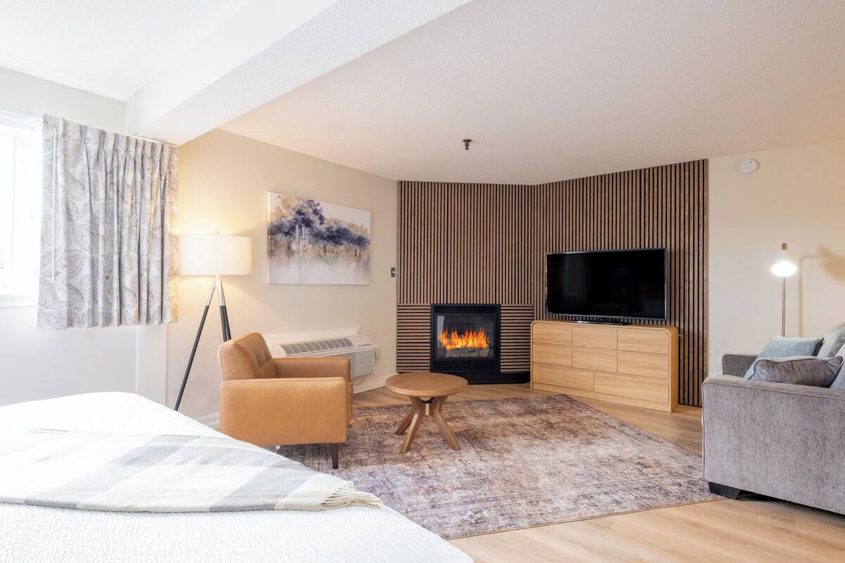 A modern living room with a fireplace, a flat-screen TV, a sofa, a chair, and a lamp.