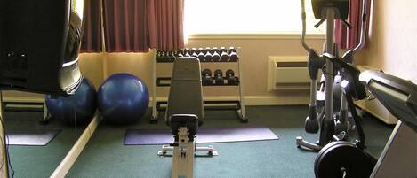 A gym with exercise equipment, a television, and a window with curtains.