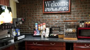 A coffee station with a 'Welcome' sign, a coffee machine, and various condiments and pastries.
