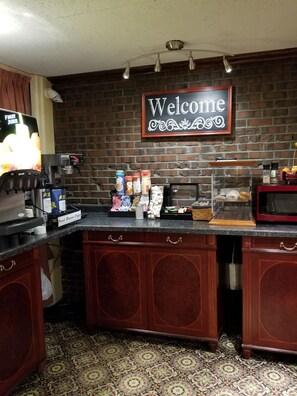 A coffee station with a 'Welcome' sign, a coffee machine, and various condiments and pastries.