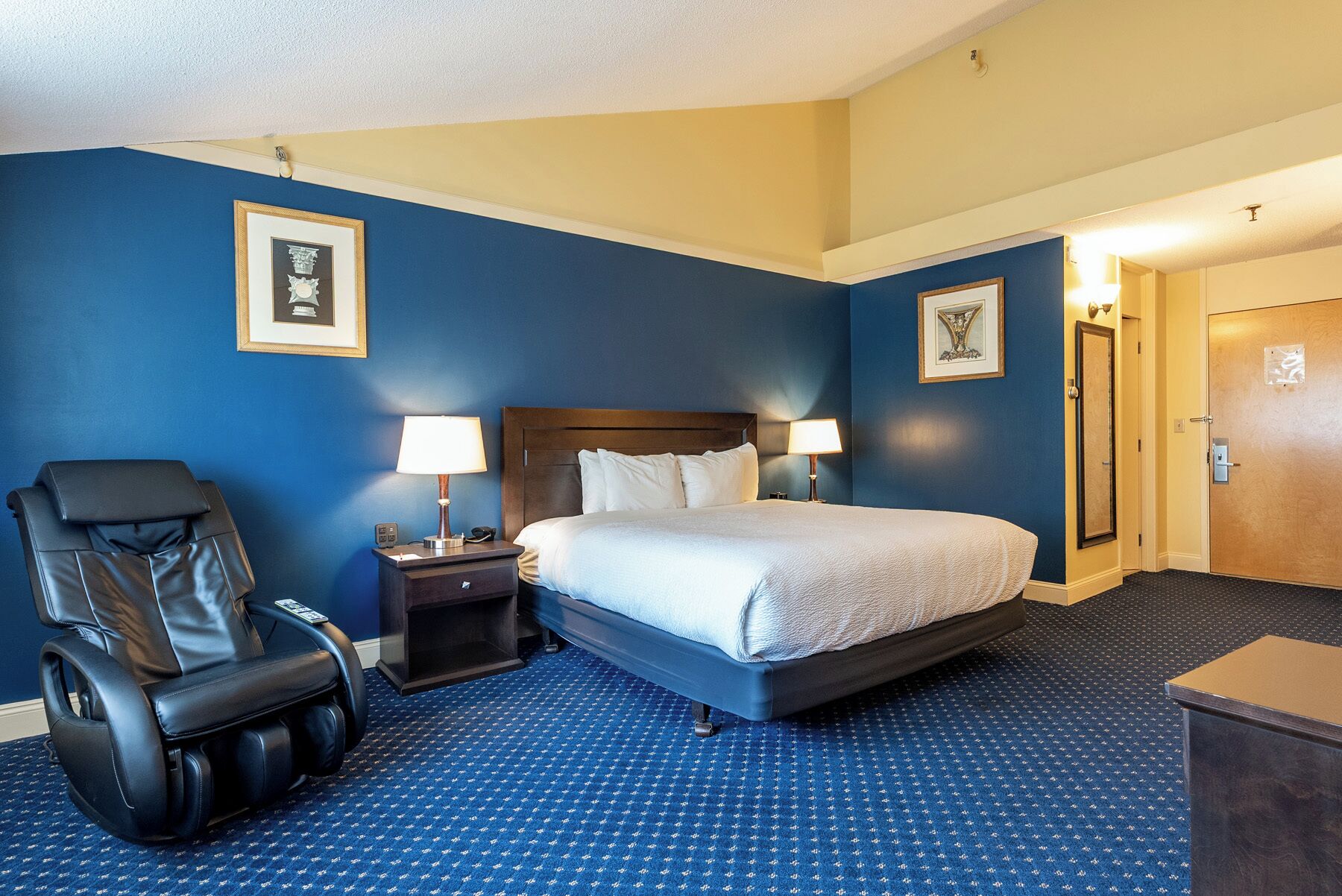 Una habitación de hotel con cama, sillón de masaje, mesita de noche y puerta.