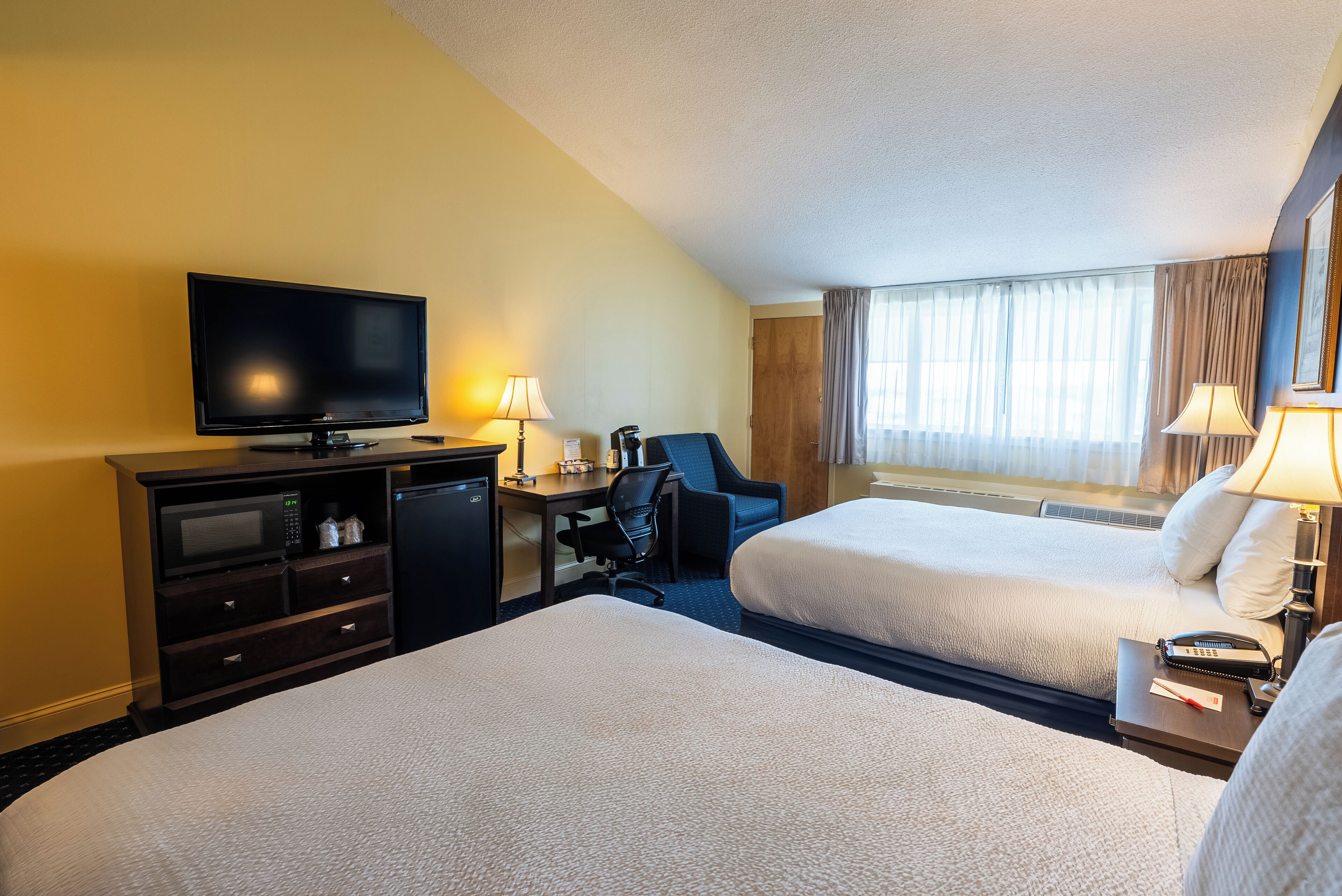 Une chambre d’hôtel avec deux lits, un bureau avec un ordinateur, une télévision et une fenêtre avec des rideaux.