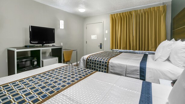 A hotel room with two beds, a TV, a desk with a computer, and a window with curtains.
