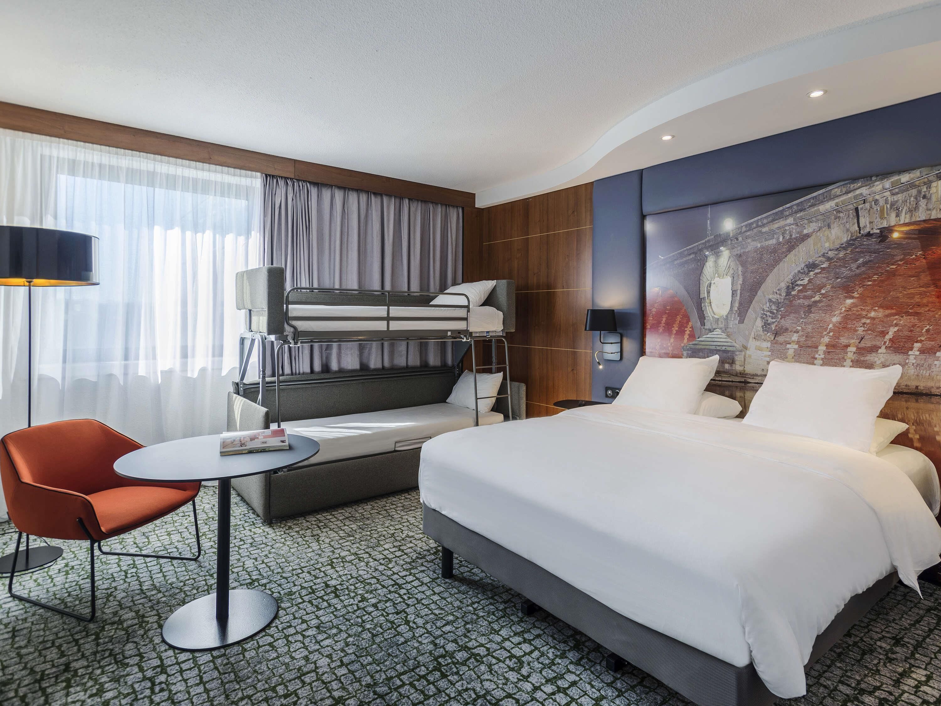 Une chambre d’hôtel avec un lit superposé, un lit simple, une table ronde, une chaise et une grande fresque murale.