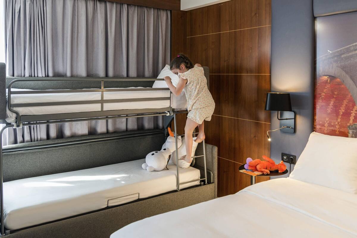 Une chambre d’hôtel avec des lits superposés, une table de chevet avec une lampe et une œuvre d’art accrochée au mur.