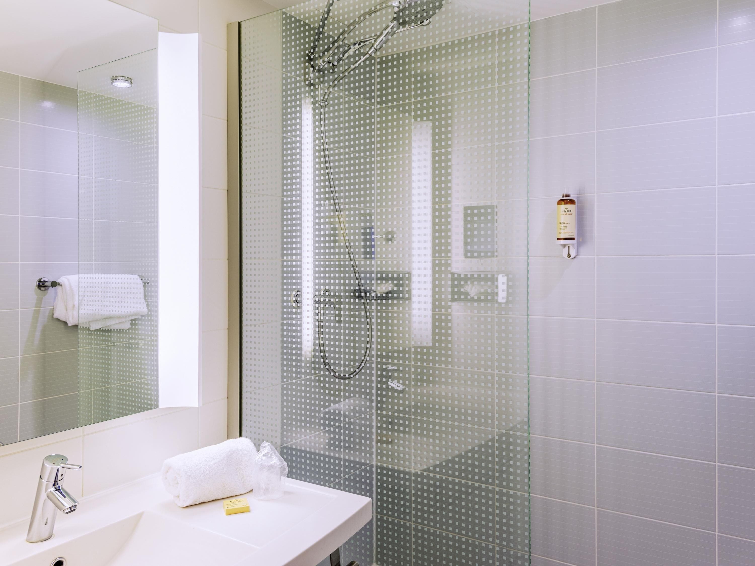 A modern bathroom with a glass shower enclosure, a white sink, and a mirror.