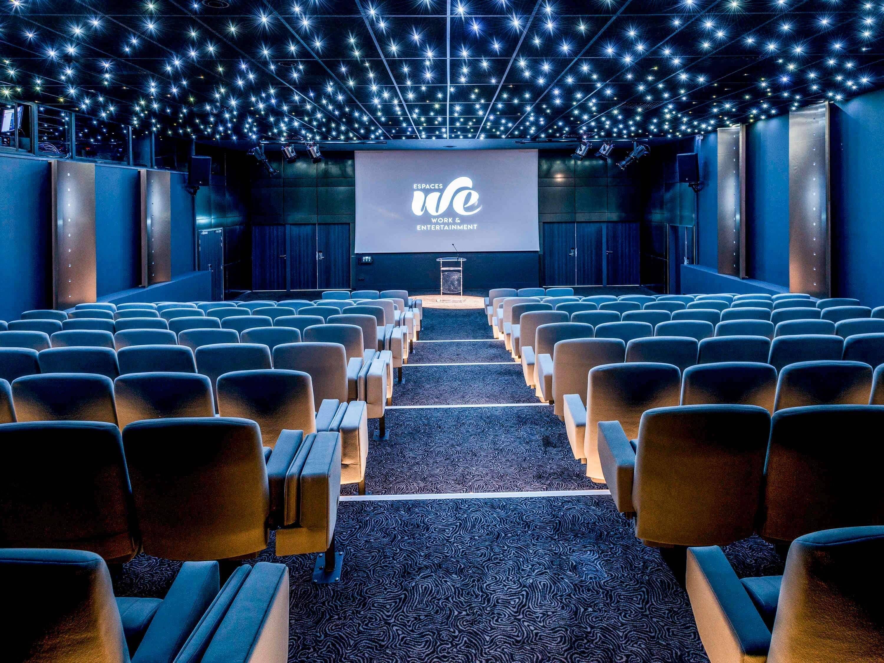 Cine con filas de asientos, una pantalla grande y un techo decorado con estrellas.