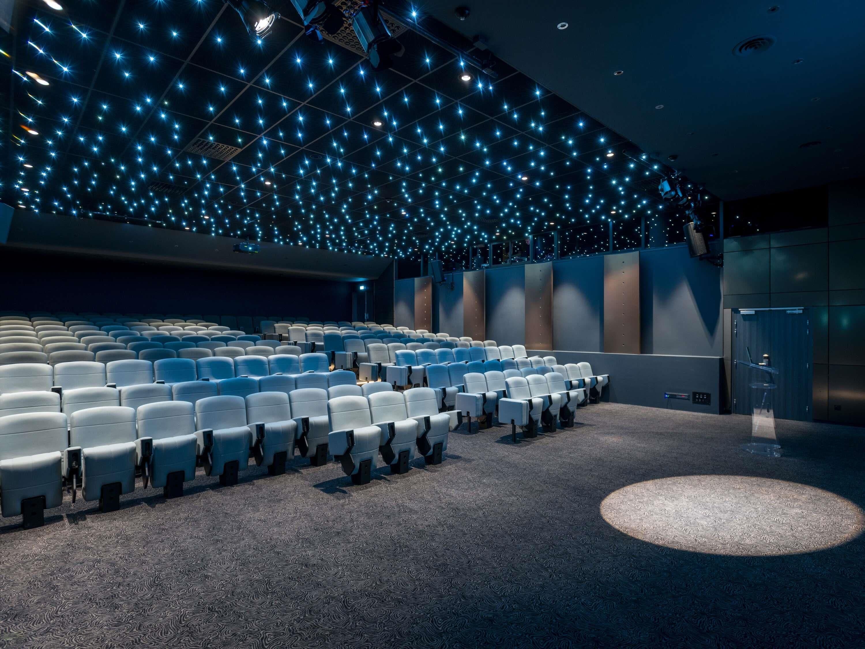 Un théâtre avec des rangées de sièges, une moquette à motifs et un plafond orné de luminaires.