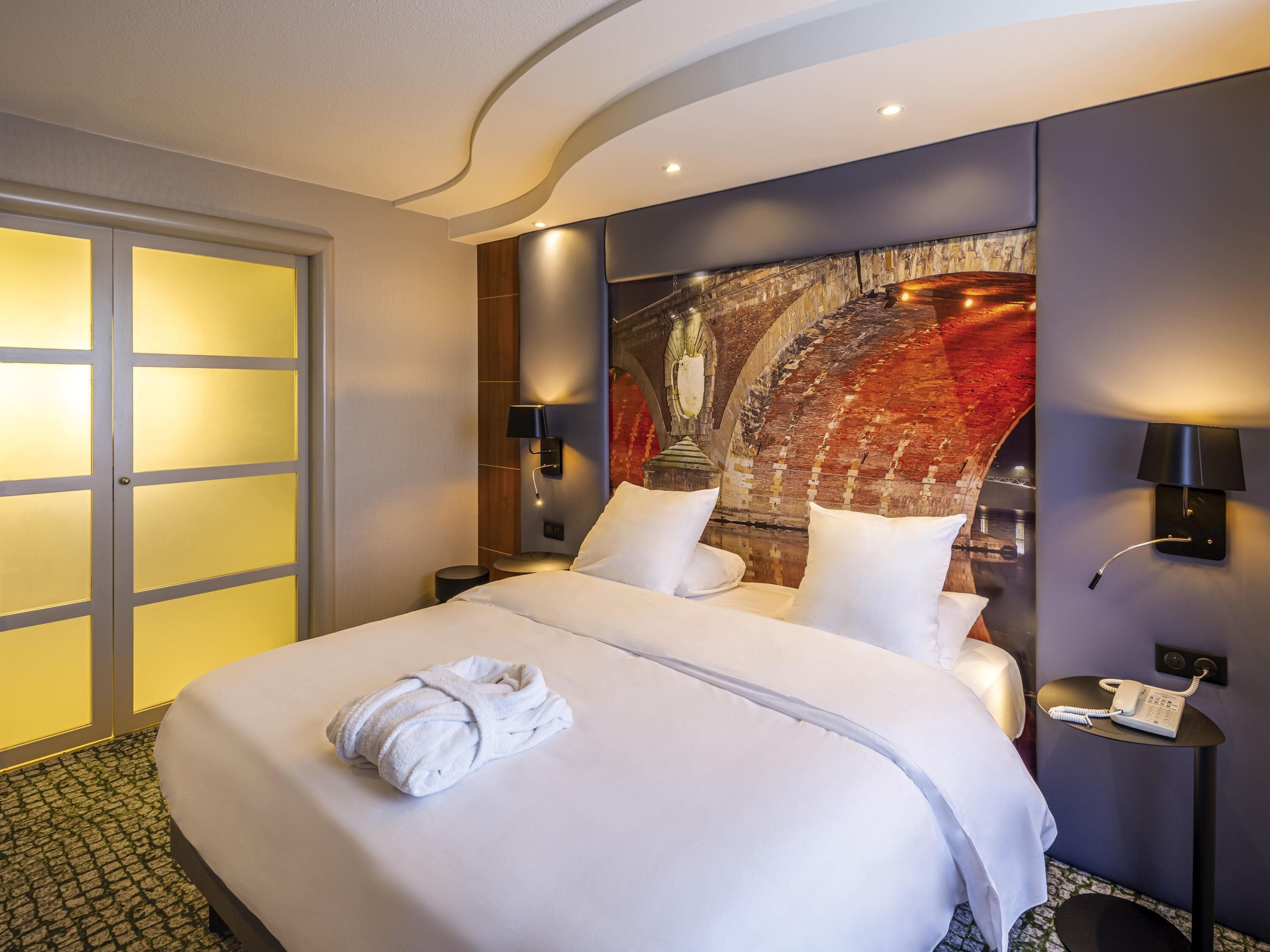 Habitación de hotel con cama, teléfono en la pared y un cuadro.