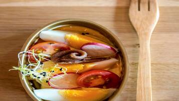 A meal in a metal bowl with various vegetables and sprouts, accompanied by a wooden fork on a wooden table.
