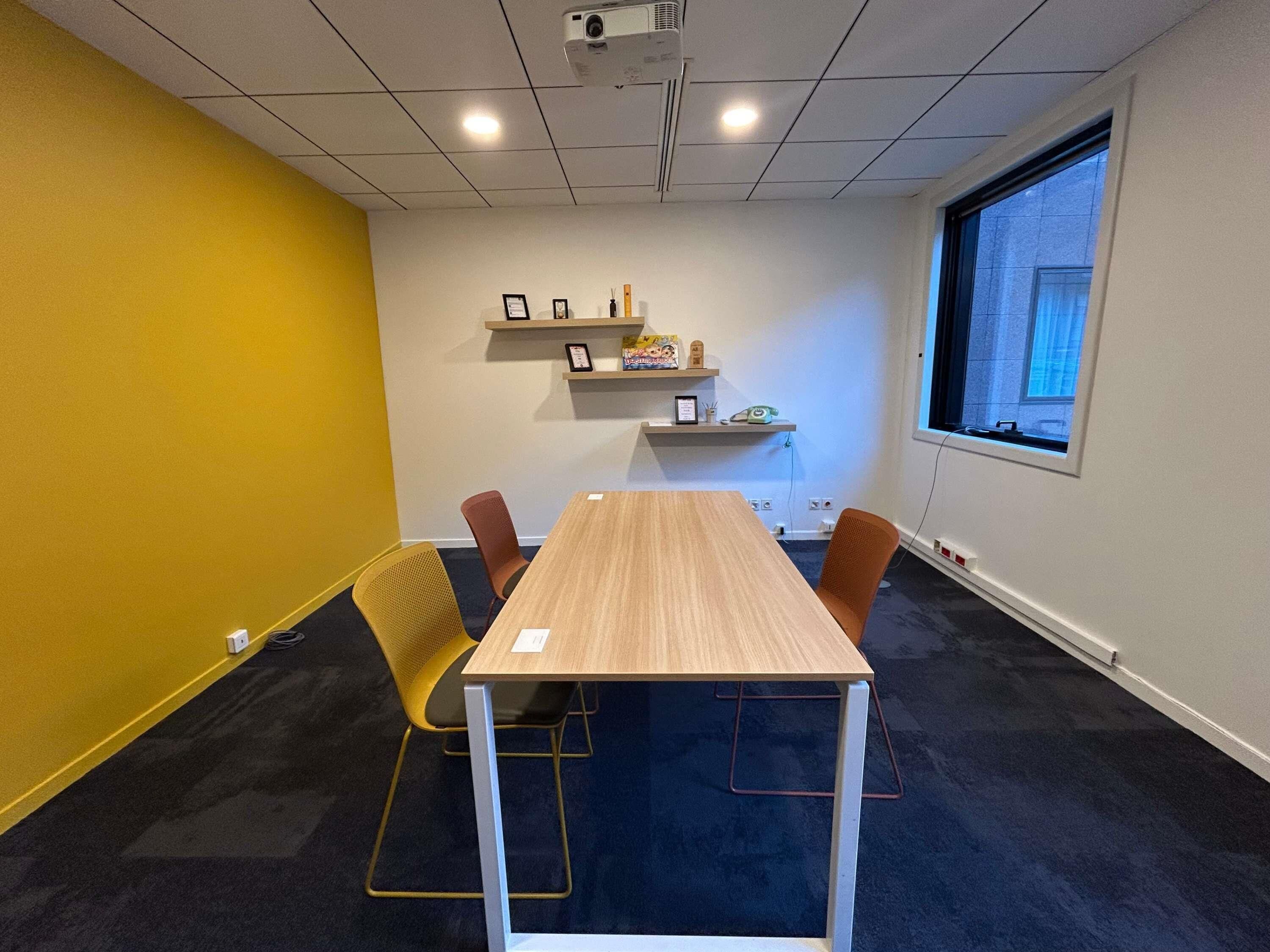 A conference room with a long table, two chairs, a projector, a window, and shelves with items.