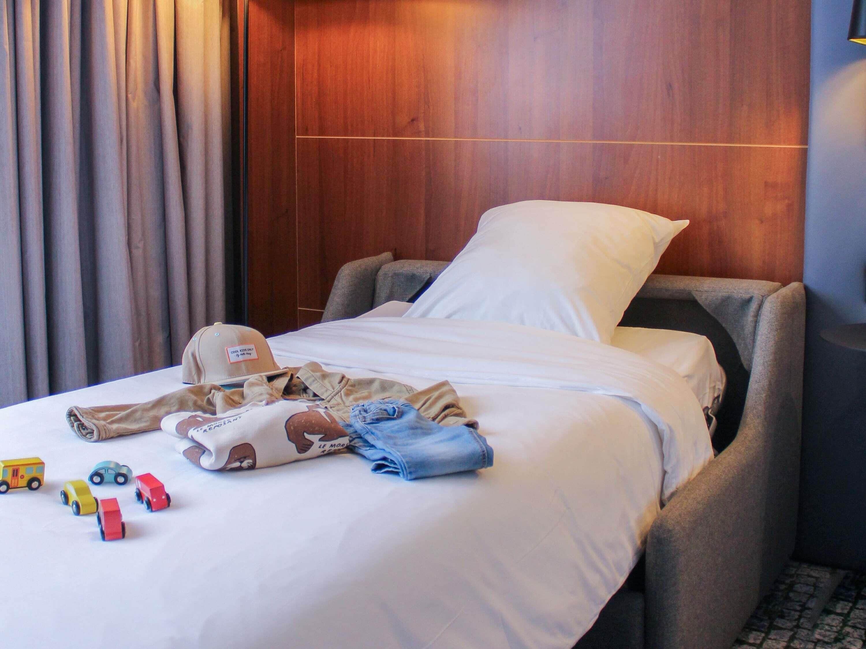 Una habitación de hotel con cama, mesita de noche y ventana con cortinas.