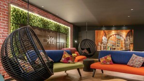 Een moderne loungeruimte met een bakstenen muur, een groene verticale tuin en kleurrijke zitplaatsen, waaronder een hangstoel en banken.