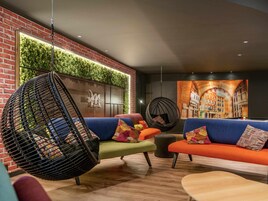 A modern lounge area with a brick wall, green vertical garden, and colorful seating including a hanging chair and sofas.