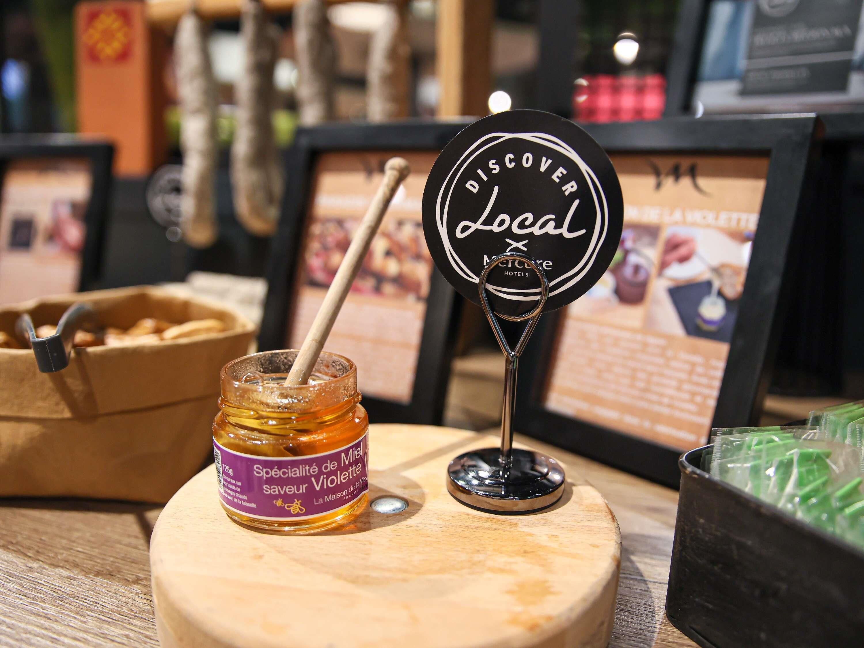 Un tarro de miel con la etiqueta 'Specialité de Miel', una señal que dice 'Discover Local' y un menú enmarcado al fondo.