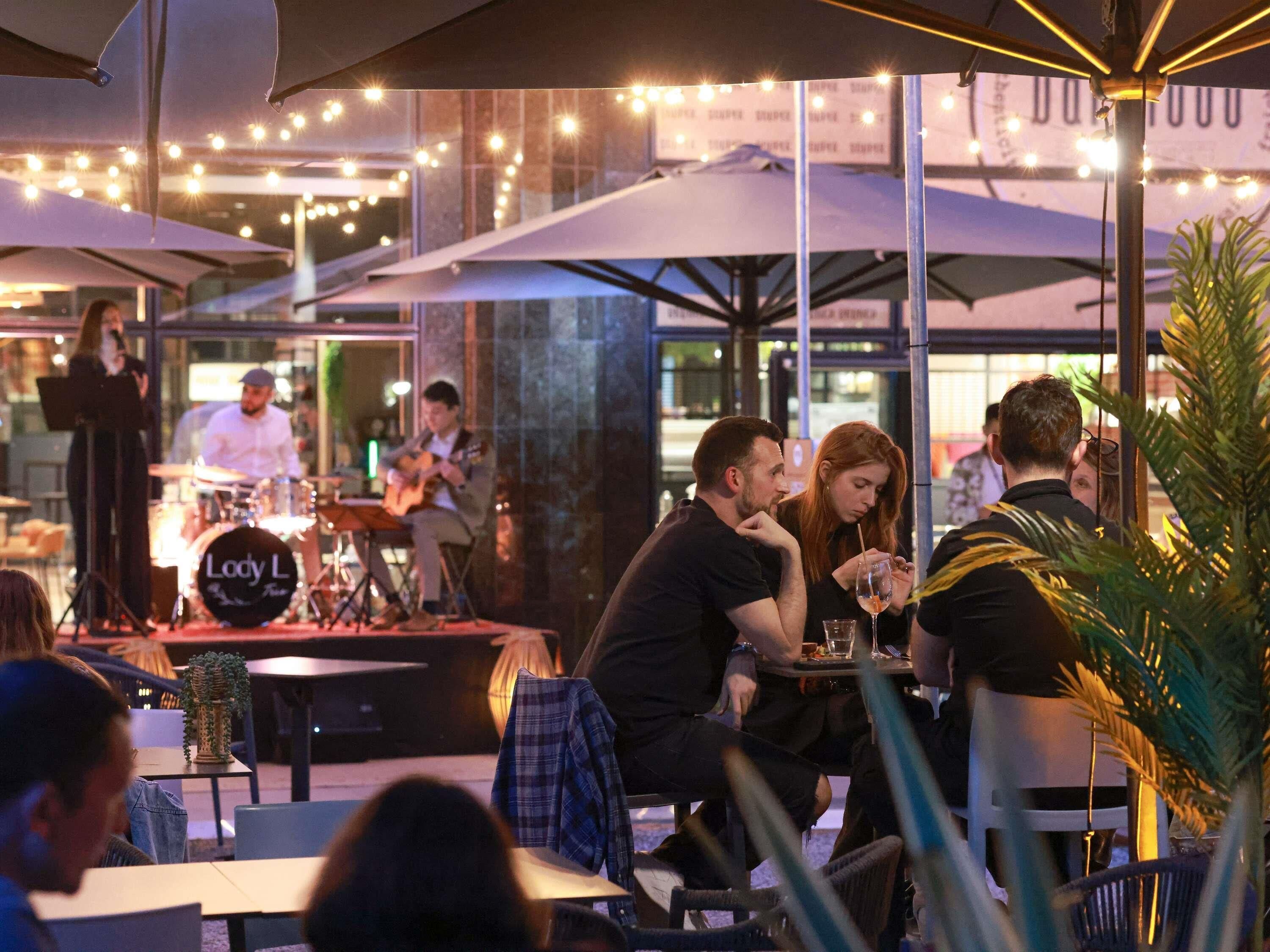 An outdoor dining area with tables and umbrellas, a stage with a band, and a sign that reads "Lady L".