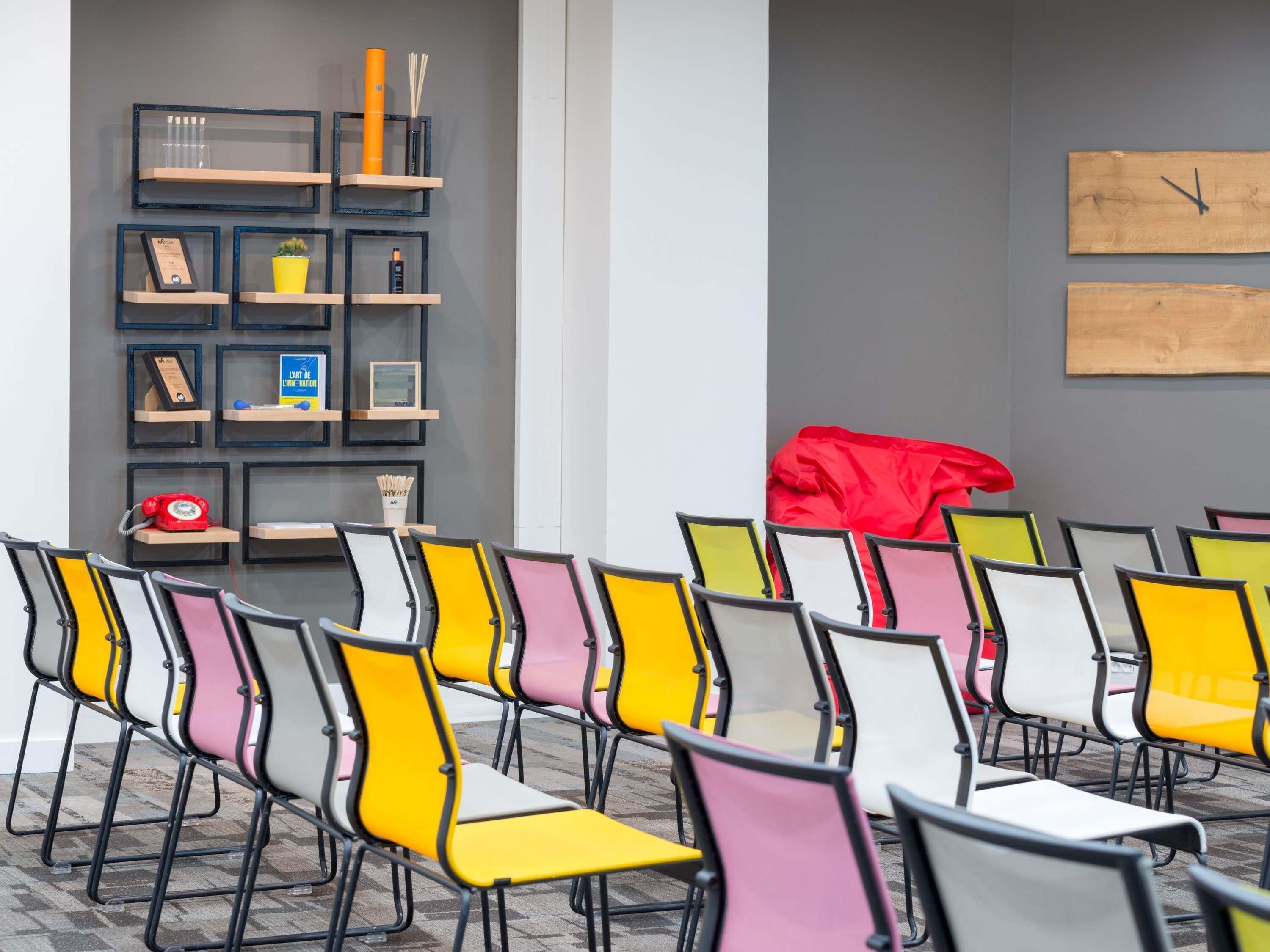 A conference room with rows of chairs, a bookshelf with various items, and a clock on the wall.