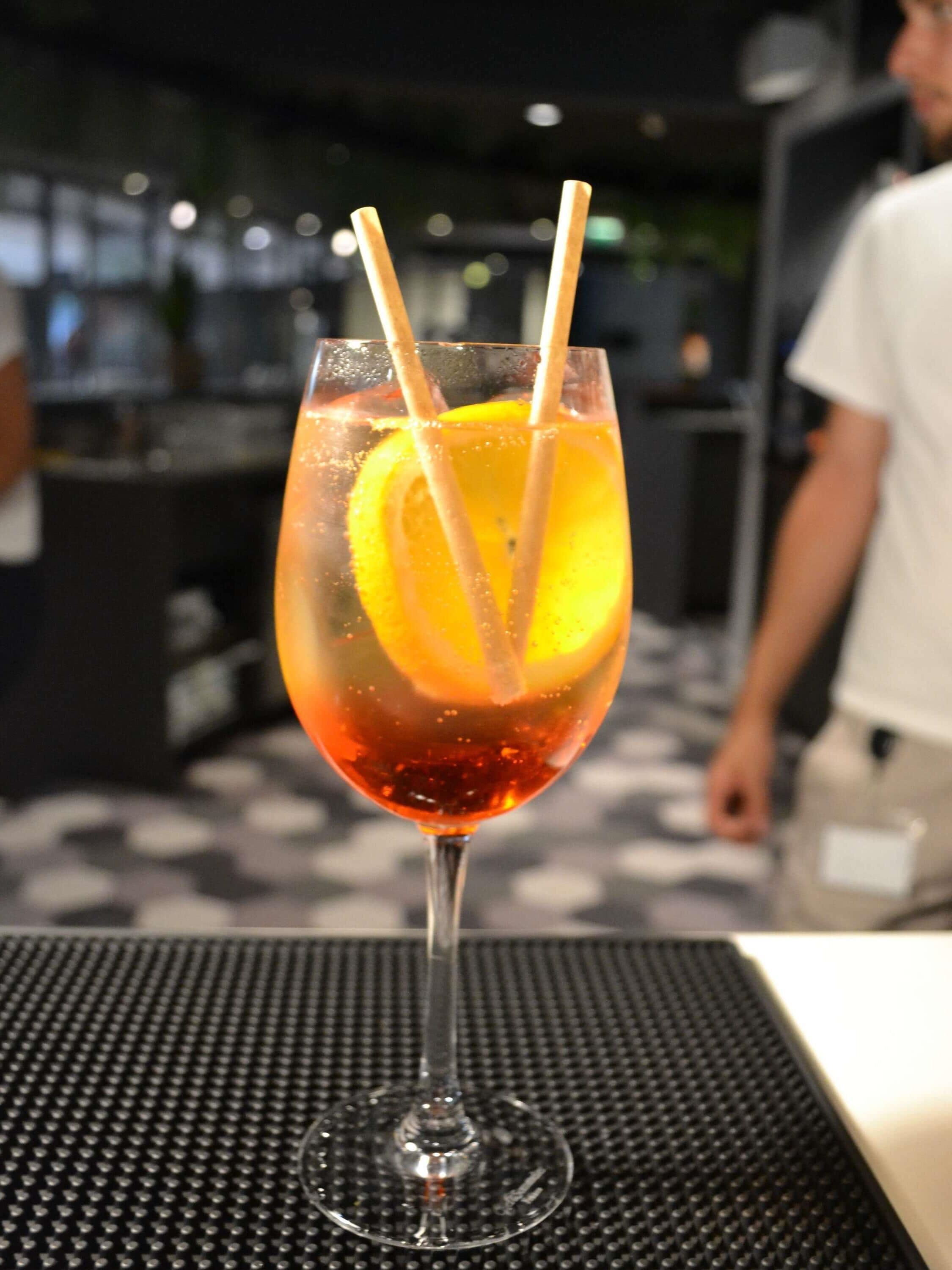 A cocktail glass with a lemon slice and two straws on a textured table.