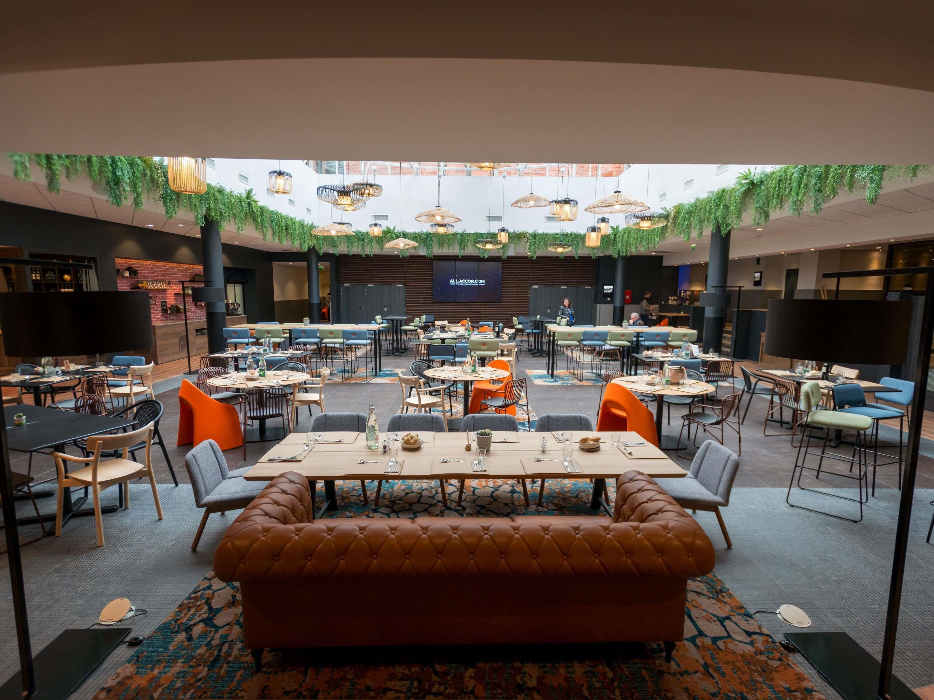 A spacious conference room with multiple tables and chairs, a central sofa, and hanging plants.