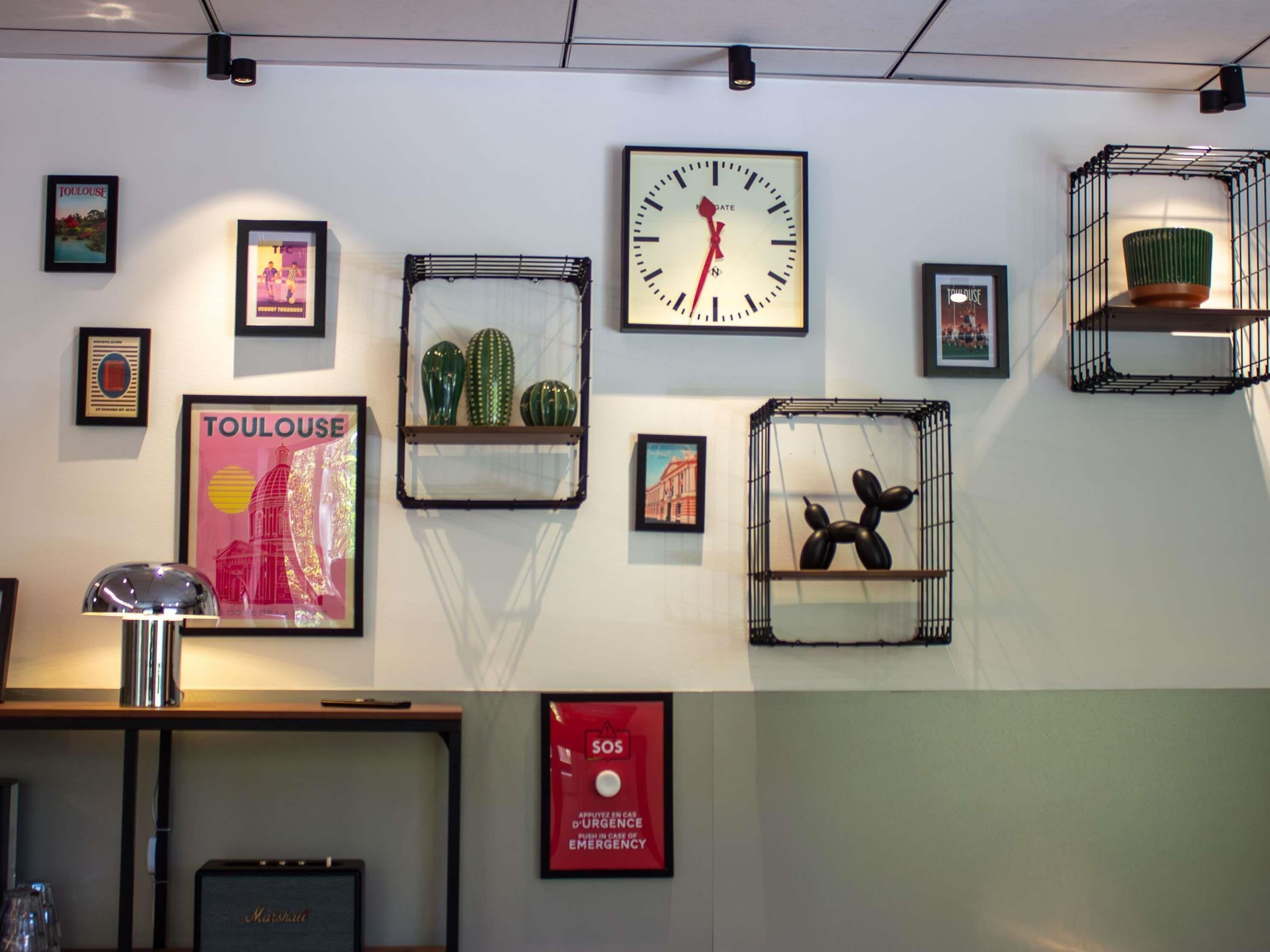 Un mur orné de divers objets encadrés, notamment une horloge, des cactus et une sculpture en forme de ballon représentant un chien.