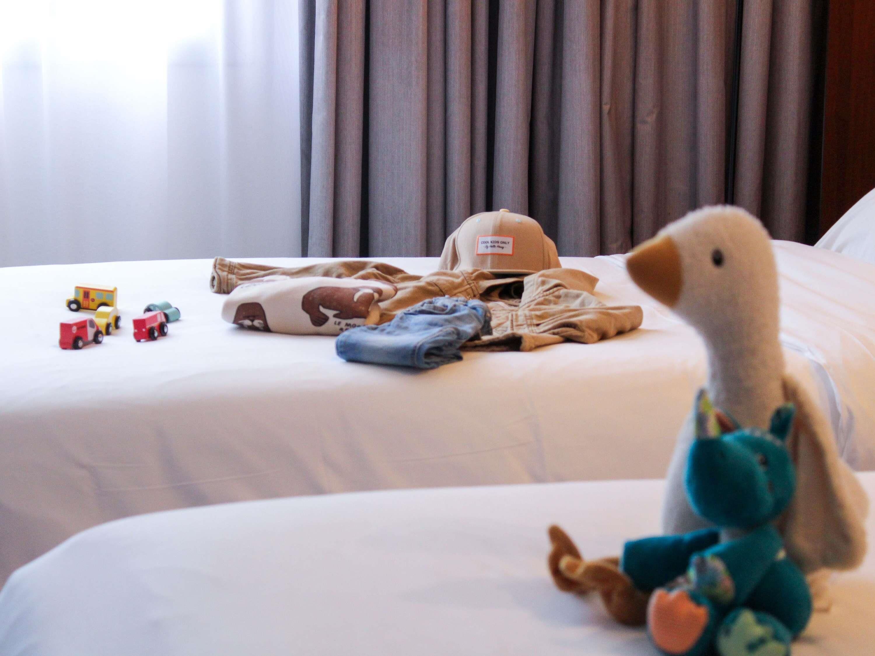 Ett hotellrum med två sängar, en mjuk gosedjursanka och barnleksaker på sängarna.