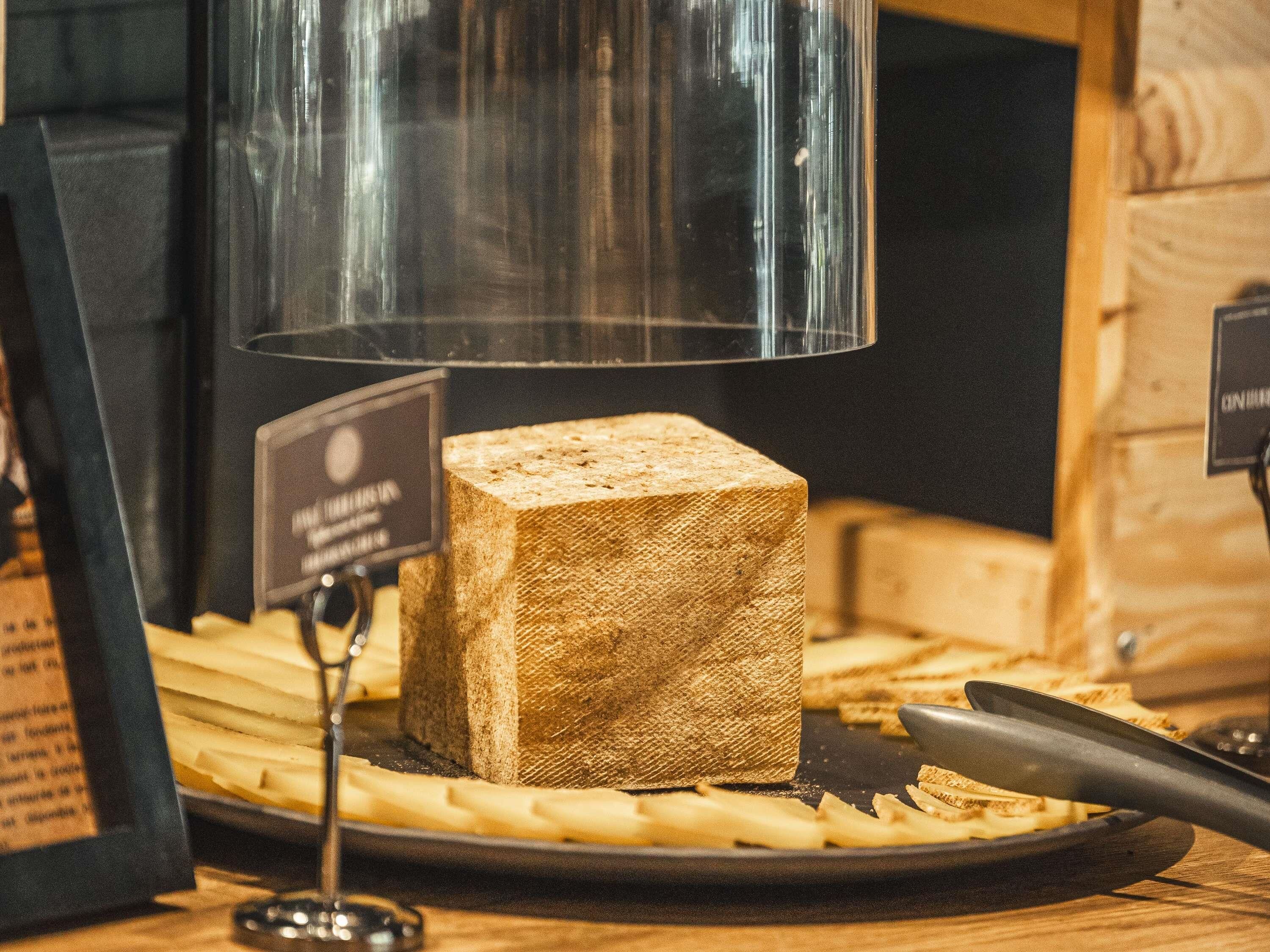 Un bloc de fromage sur une planche en bois, avec une étiquette, un couteau et un récipient en verre en arrière-plan.