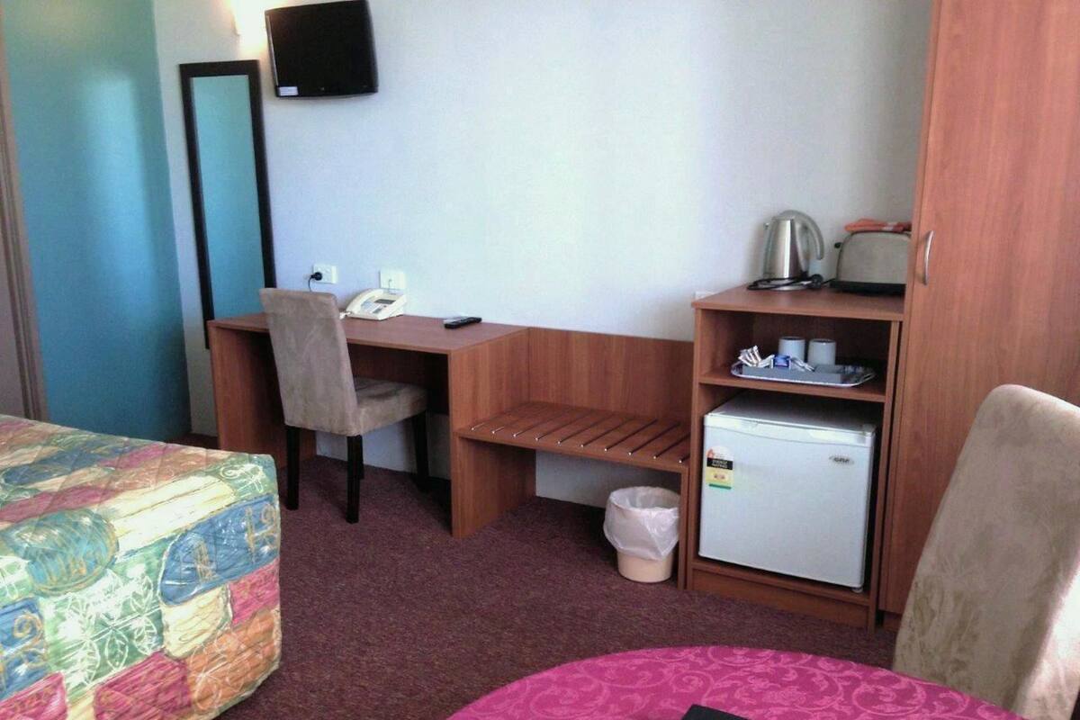 A hotel room with a bed, a desk, a chair, a small refrigerator, and a TV mounted on the wall.