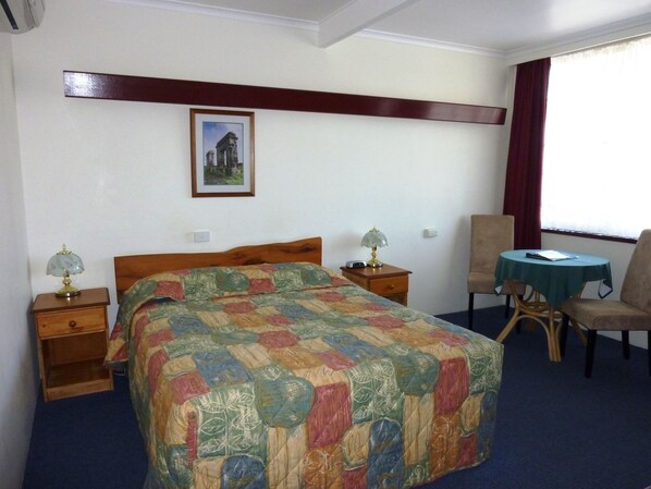 A hotel room with a bed, two bedside tables with lamps, a chair, a small table, and a window with curtains. - Mountain View Country Inn (Deloraine)
