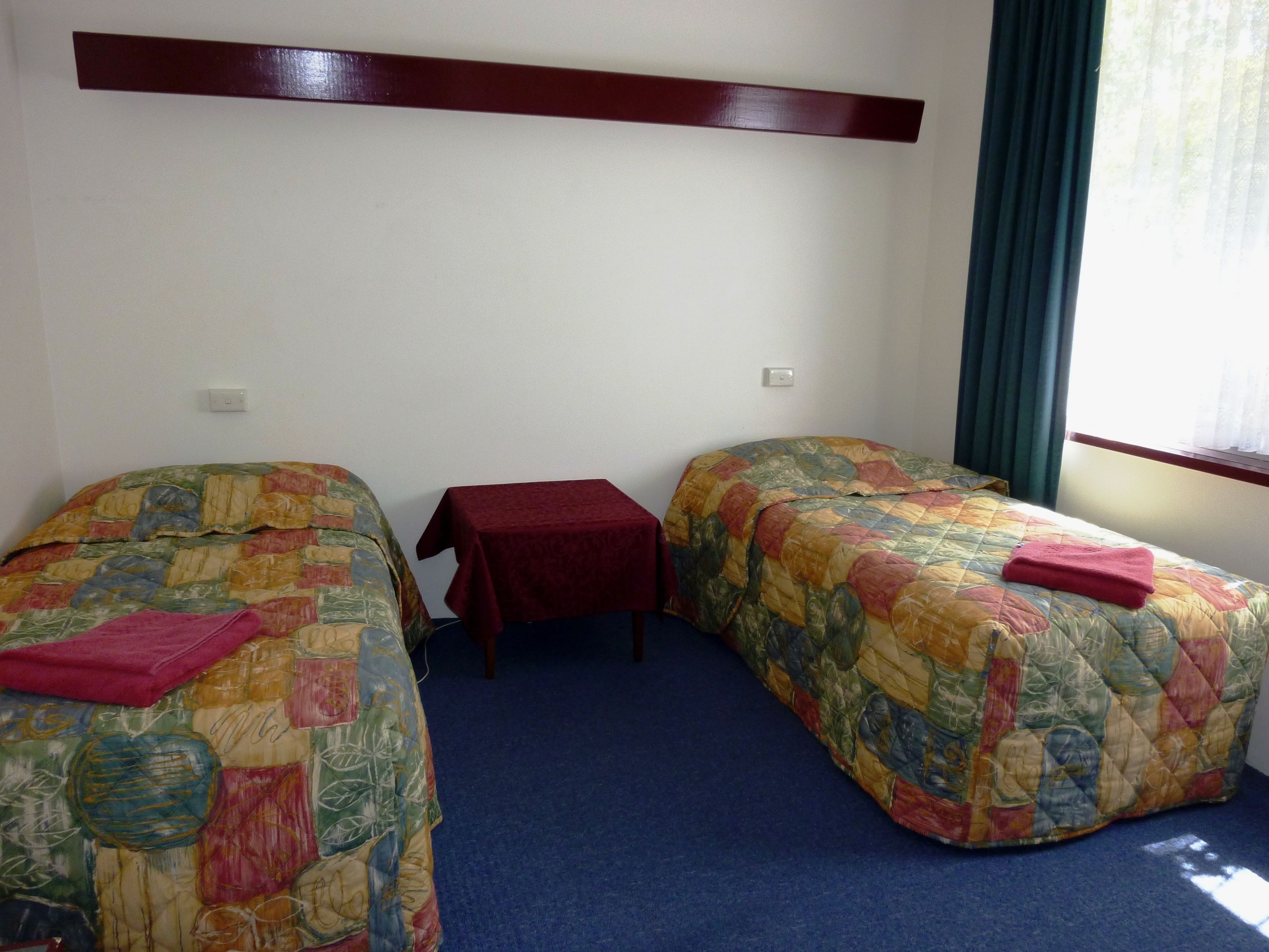 A hotel room with two single beds, a small table, and a window with curtains.