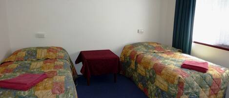 Een hotelkamer met twee enkele bedden, een tafeltje en een raam met gordijnen.
