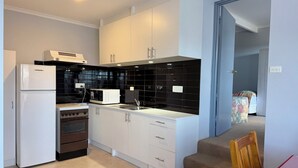Uma cozinha moderna com armários brancos, painel de azulejos pretos, geladeira branca, micro-ondas e forno.