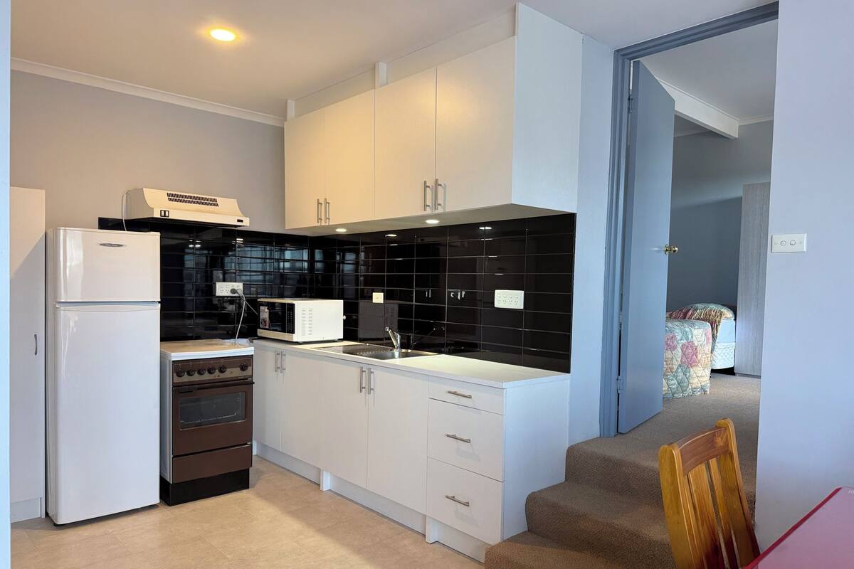 A modern kitchen with white cabinets, a black tiled backsplash, a white refrigerator, a microwave, and an oven.