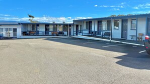 A motel with a parking lot, outdoor seating, and a clear sky.