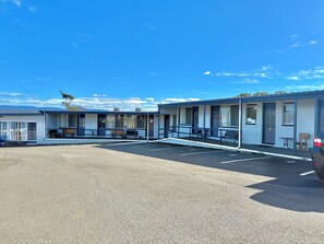 A motel with a parking lot, outdoor seating, and a clear sky.